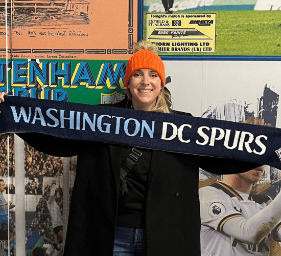 Board member Rachel holding DC Spurs scarf at Tottenham Hotspur Stadium.